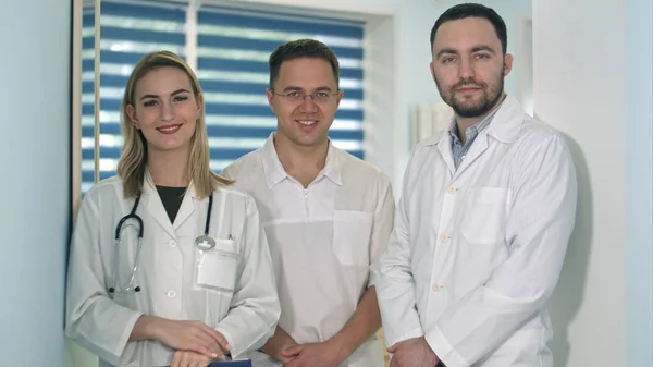 Двоє чоловіків-лікарів і жінка-лікар зі стетоскопом посміхаються до камери — стокове фото
