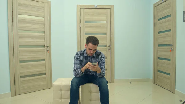 Paciente masculino usando el teléfono mientras espera su cita con el médico — Foto de Stock