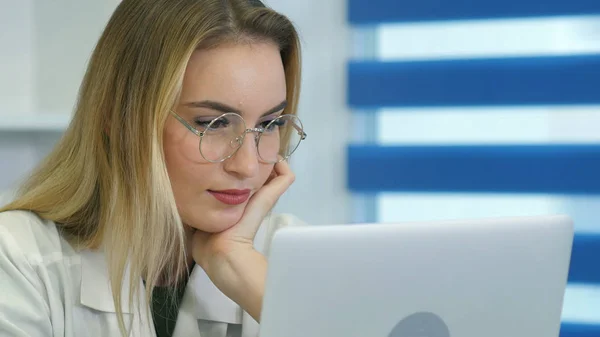 Enfermera joven en gafas usando portátil en el escritorio en el consultorio médico — Foto de Stock