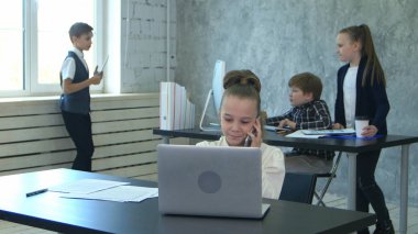 Küçük iş kız telefonla iletişim kurar ve dizüstü bilgisayar bakar