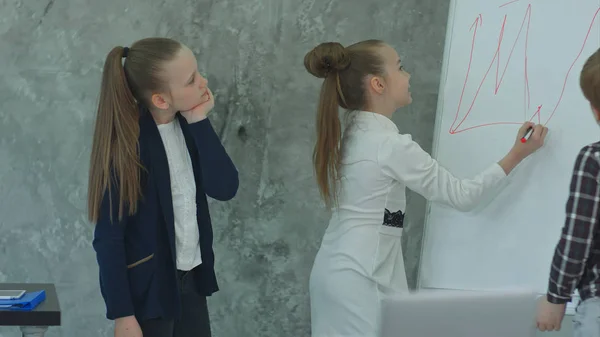 Jovem menina de negócios desenhando em flipchart no escritório, discutindo com pequenos colegas — Fotografia de Stock