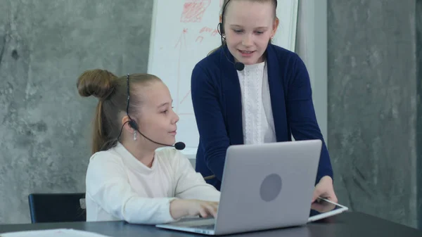 Dość dwa dziewczynka w zestaw słuchawkowy za pomocą laptopa i flipchart w biurze — Zdjęcie stockowe