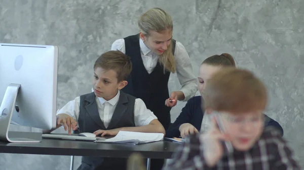 Tre bambini piccoli in abiti da lavoro seduti a tavola con il computer portatile, discutendo qualcosa — Foto Stock