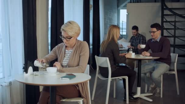 Νεαρή όμορφη γυναίκα κάθεται στο τραπέζι και πίνοντας καφέ εσωτερική — Αρχείο Βίντεο