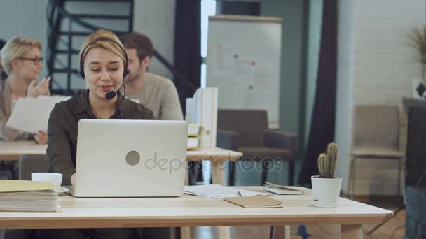 Retrato de una hermosa mujer de negocios trabajando en su escritorio con auriculares y portátil — Vídeos de Stock