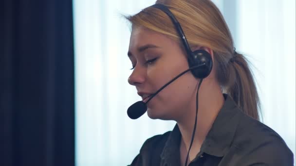 Operadora de atención al cliente femenina con auriculares hablando y sonriendo — Vídeo de stock