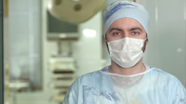 Zkušený mladý chirurg, vážný muž nosí masku při pohledu do kamery — Stock video
