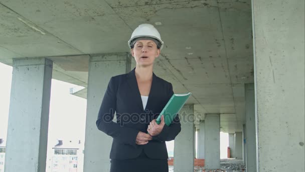 Female construction manager with blueprint on building site presenting the project looking at camera — Stock Video