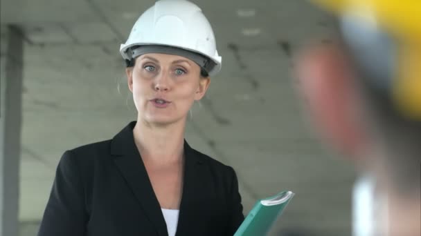 Μια γυναίκα νεαρός αρχιτέκτονας που εργάζεται σε εργοτάξιο, μιλώντας με τον συνάδελφό της — Αρχείο Βίντεο