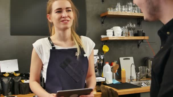Portréja egy gyönyörű női barista figyelembe a megrendelés a vevő, egy tabletta számítógép, és mosolyogva — Stock videók