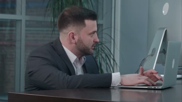 Empresário caucasiano atraente usando laptop, enquanto conversa com o parceiro no local de trabalho — Vídeo de Stock