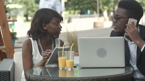 Hombre y mujer de negocios afroamericanos trabajando juntos en la cafetería moderna, teniendo llamadas telefónicas, usando computadora portátil y tableta digital — Vídeo de stock