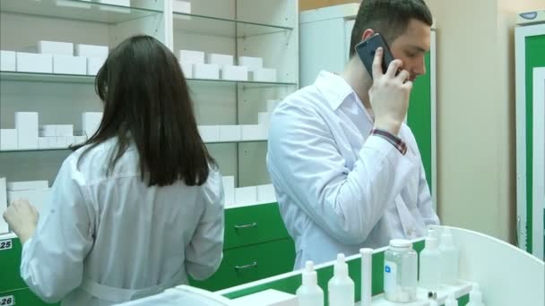 Joven farmacéutico masculino hablando por teléfono móvil mientras comprueba la prescripción en farmacia — Vídeos de Stock