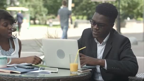 Afrikai férfi és női kolléga dolgozik együtt, Minialkalmazások használata ülésen egy kávézóban — Stock videók