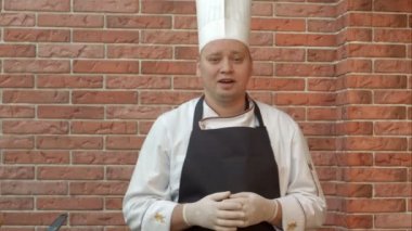 Gülümseyen aşçı kameraya yemek hazırlamak için gidiyor hakkında konuşurken kitchennd ayakta