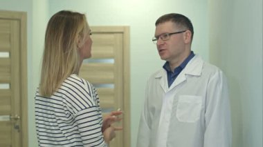 Erkek doktor hastane koridorunda genç bir hastayla konuşuyor.