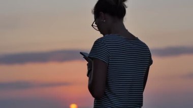 Smartphone cep telefonu ile sahilde günbatımı sırasında kadın manifatura