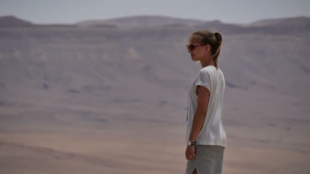 Mujer joven en gafas de sol de pie en los acantilados borde y mirando alrededor del desierto — Vídeos de Stock