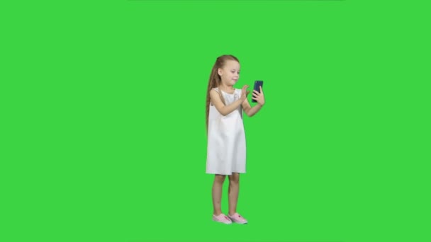 Niedliches kleines Mädchen benutzt ein Smartphone und lacht auf einem grünen Bildschirm, Chroma-Taste — Stockvideo