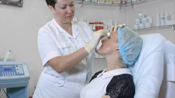 Le mani di estetista in guanti di gomma puliscono la pelle di cliente femminile in salone di bellezza — Video Stock