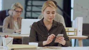 Onun çalışma evinde otururken gülümseme ile onun akıllı telefon kullanan neşeli genç güzel kadın