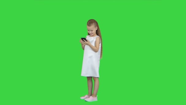 Schattig klein meisje glimlachen en maakt gebruik van een mobiele telefoon op een groen scherm, Chroma Key — Stockvideo