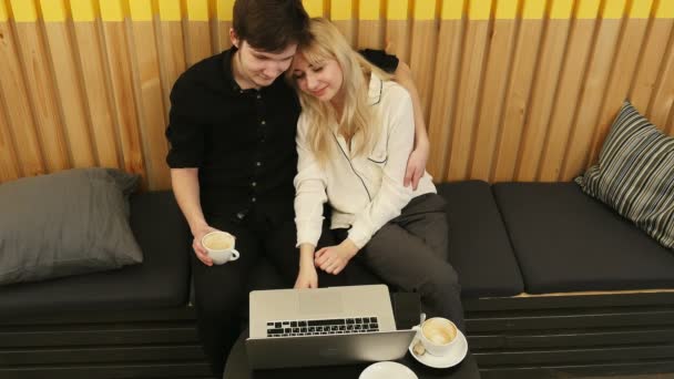 Atractiva pareja joven usando una computadora portátil para ver su programa de televisión favorito en la cafetería — Vídeo de stock