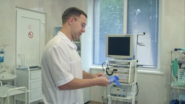 Cirujano masculino que se pone guantes de goma estériles para la cirugía mientras se lava las manos en una sala de cirugía — Vídeos de Stock
