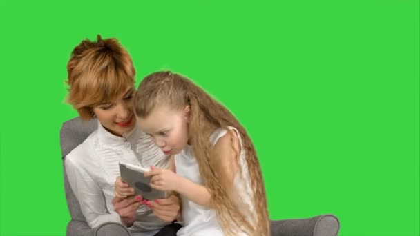 Ung mor och hennes dotter sitta tillsammans och titta på tabletten på en grön skärm, Chroma Key — Stockvideo