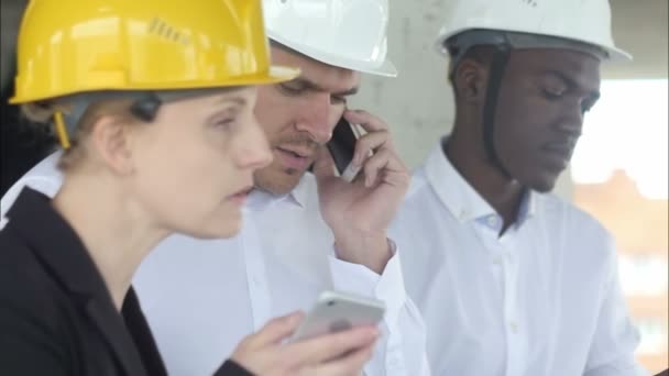 Reunión de ingenieros en la terraza del sitio de construcción, discutiendo el plan y teniendo llamadas telefónicas — Vídeo de stock