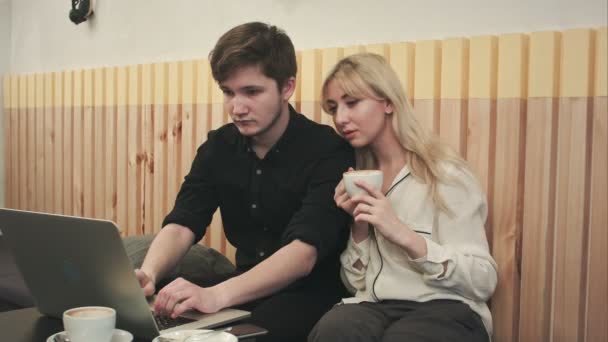 Пара працює на ноутбуці, п'є каву в кафе — стокове відео