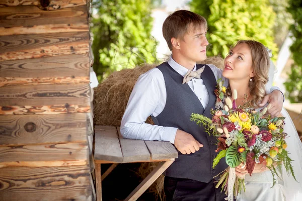 De bruid in een witte jurk en bruidegom gilet staande groene tuin — Stockfoto