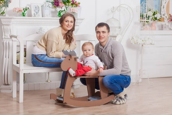 Balanço de cavalo de madeira do bebê perto da árvore decorada de natal com os pais — Fotografia de Stock