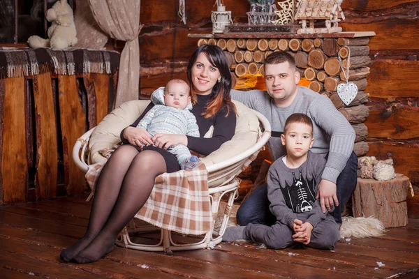 Familia joven con dos niños cerca de la chimenea celebrando la Navidad —  Fotos de Stock