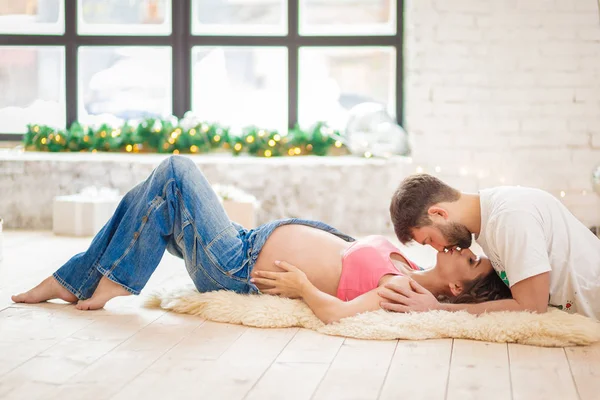 Homme affectueux embrasser sa femme enceinte avec des lettres de bébé sur le ventre couché sur le canapé à la maison — Photo