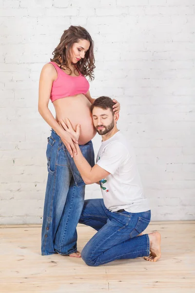 Feliz pai de família e mãe grávida e perto de uma parede de tijolo em branco no quarto — Fotografia de Stock