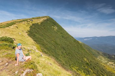 Genç bir kadın kayanın üzerinde oturuyor.