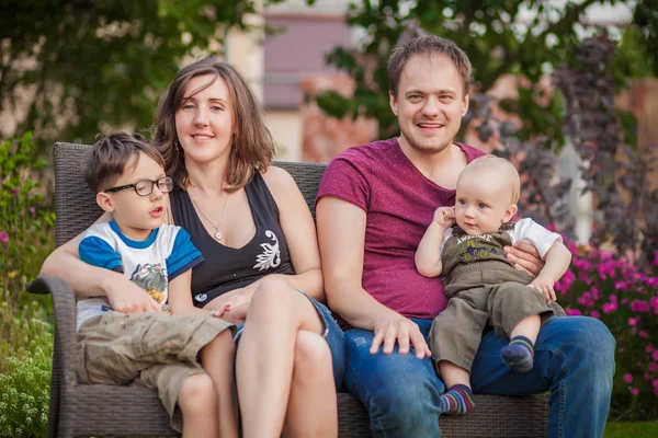 Família jovem com dois filhos sentados no banco — Fotografia de Stock