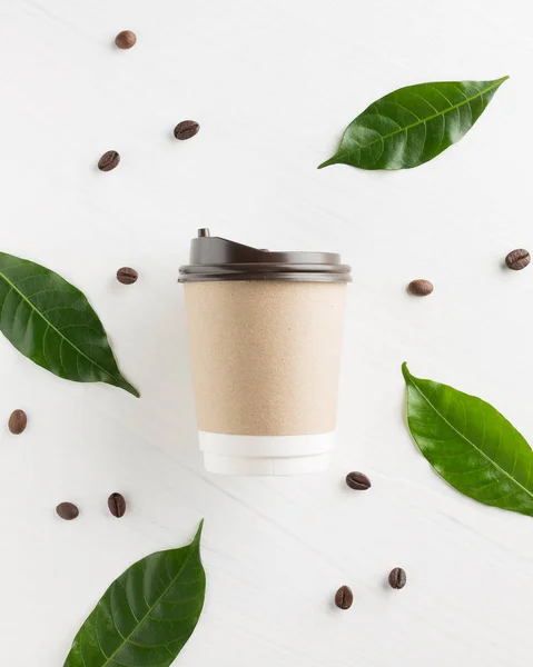 Бумажная чашка кофе с кофейными зёрнами и лист на белой деревянной спине — стоковое фото