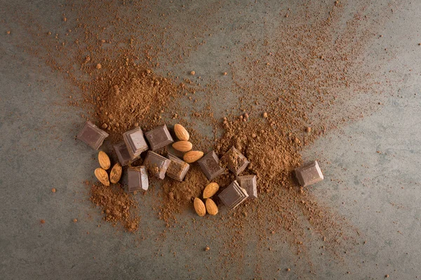 Broken chocolate pieces with cocoa powder and almond on stone ba — Stock Photo, Image