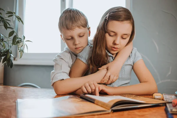 El niño y la niña leyendo libro en casa durante la cuarentena CoVid-19, aprendizaje a distancia en línea con un ordenador portátil, un niño haciendo la tarea para la escuela. Los niños se quedaron en casa . — Foto de Stock