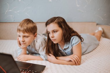 Kız ve oğlan evde dizüstü bilgisayarda CoVid-19 karantinası sırasında webinar izliyorlar. Uzaktan öğrenmeyi bilgisayarla öğreniyorlar. Okul için ödev yapan bir çocuk. Çocuklar evde kaldı. Evde eğitim