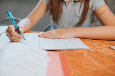 Kız evde CoVid-19 karantinası sırasında bir deftere ödev yazıyor. Uzaktan öğrenmeyi bilgisayarla yapıyor. Okul için ödev yapan bir çocuk. Çocuklar evde kaldı. Kız Kiril alfabesiyle yazıyor.