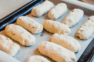 Kuru üzümlü çiğ peynirli çörekler pişirme tepsisinin üzerinde yatıyor. Çiğ hamur. Pişmemiş çörekler.