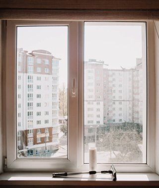 Gündüz vakti kirli camlı pencere. Pencere pervazında pencere temizleyicisi var. Pencerenin yarısını temizle
