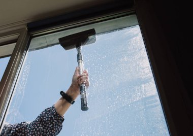 Cam temizleyicisi camları silmek için cam sileceği kullanıyor. Mavi gökyüzü.