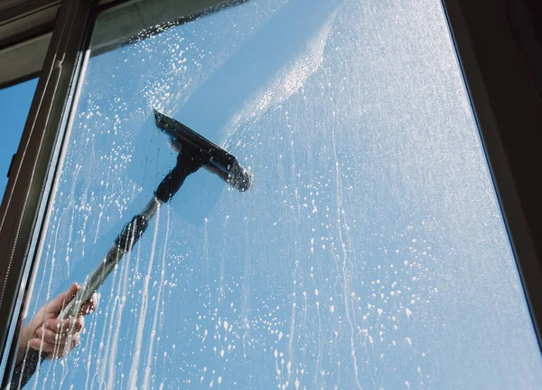 Window cleaner using a squeegee to wash a window. Outside. Daylight