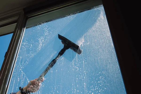 Window cleaner using a squeegee to wash a window. Blue sky.