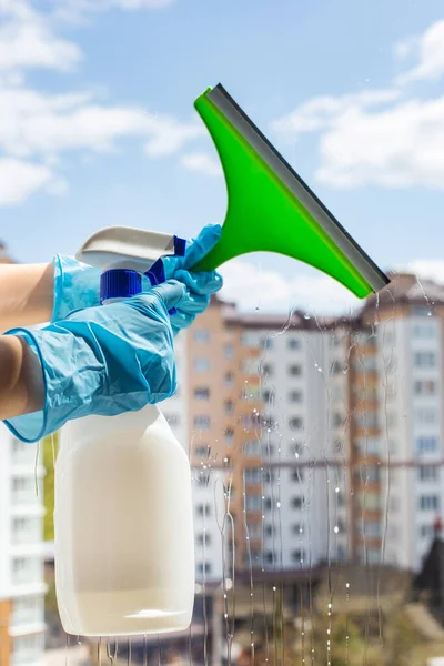 Las manos de las mujeres en guantes de goma azul brillante lavan ventanas con limpiaparabrisas y un pulverizador para lavar ventanas — Foto de Stock