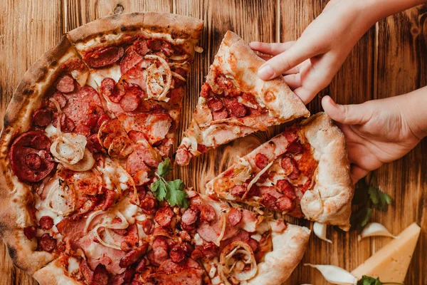 Kids eat pizza with salami and mozzarella . Flat-lay of people cutting and eating Italian pizza over wooden table, top view